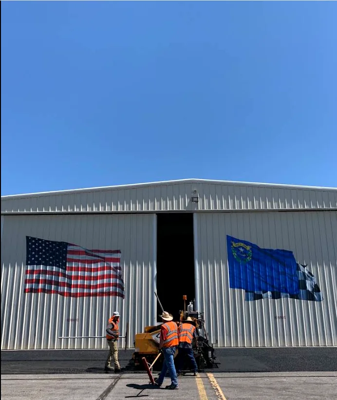 Crew paving in front of a commercial hangar building